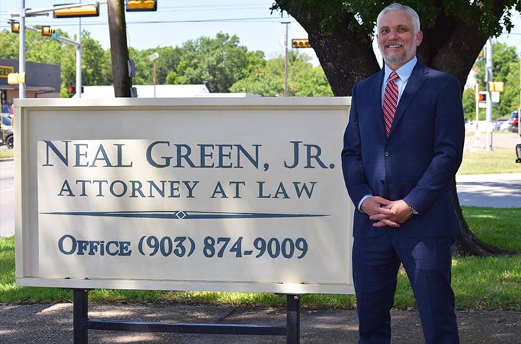 Neal Green Jr. standing next to his office sign